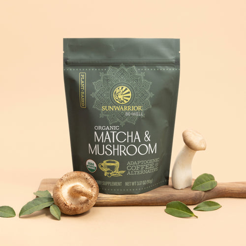 Sunwarrior organic matcha and mushroom powder supplement pouch with fresh mushrooms and green leaves on wood